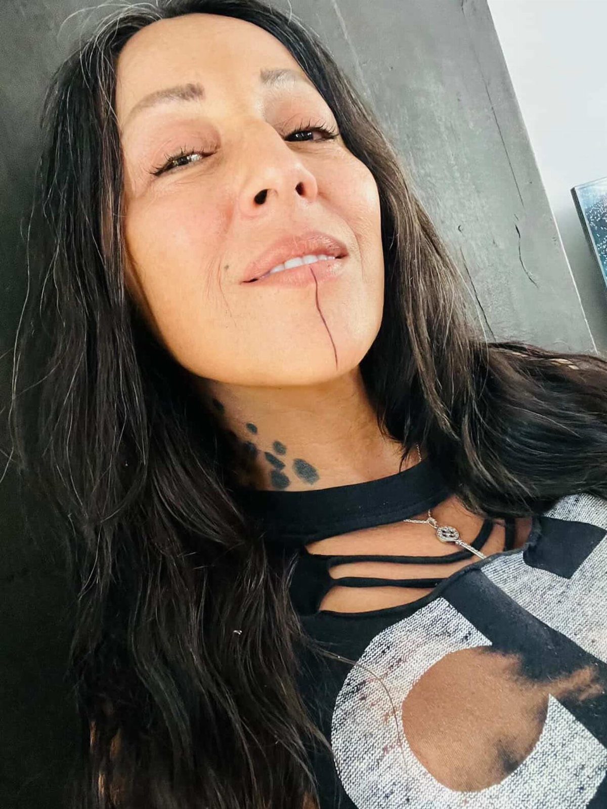 Woman with long dark hair featuring a vertical line tattoo on her chin.
