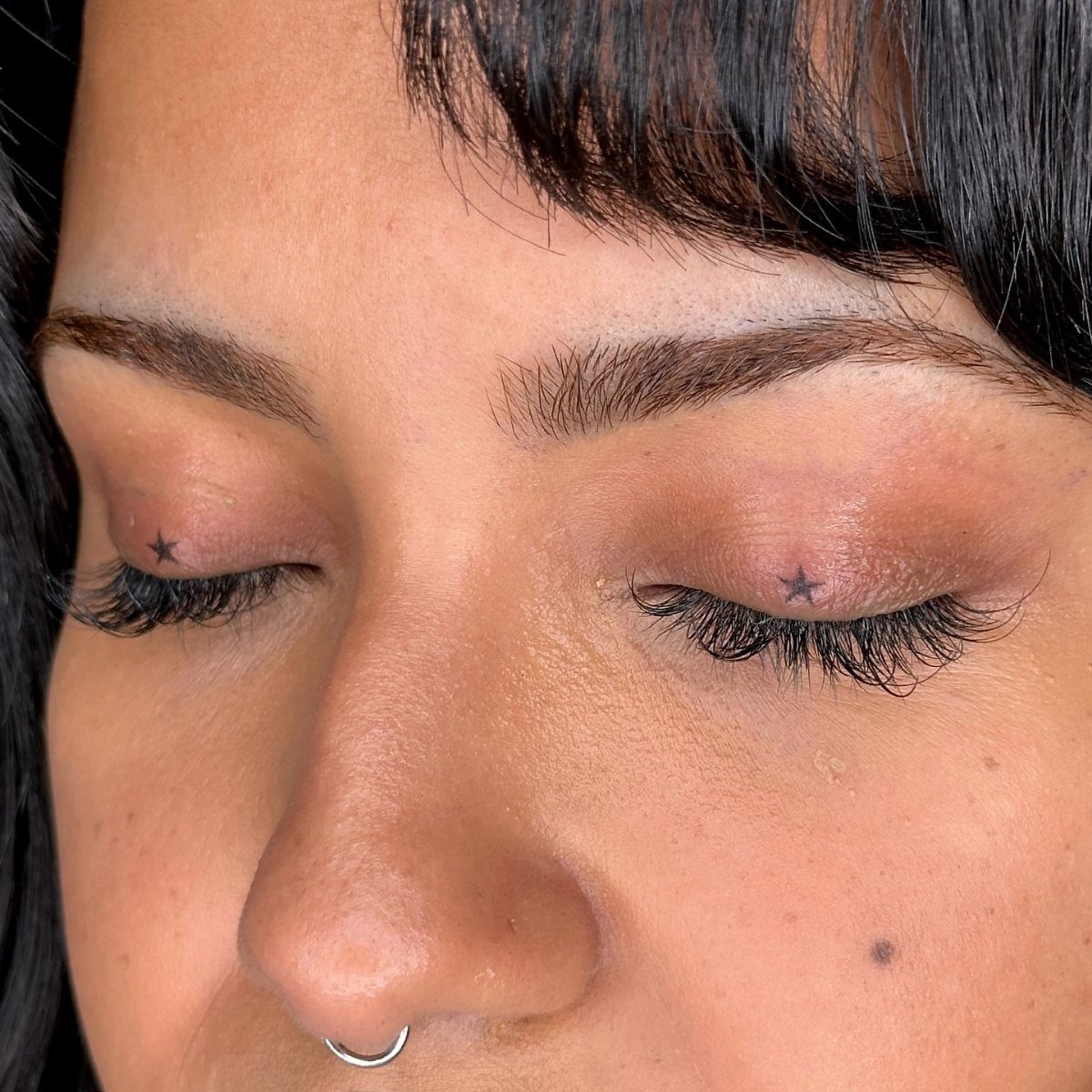 Person with closed eyes showing small black star tattoos on each eyelid.