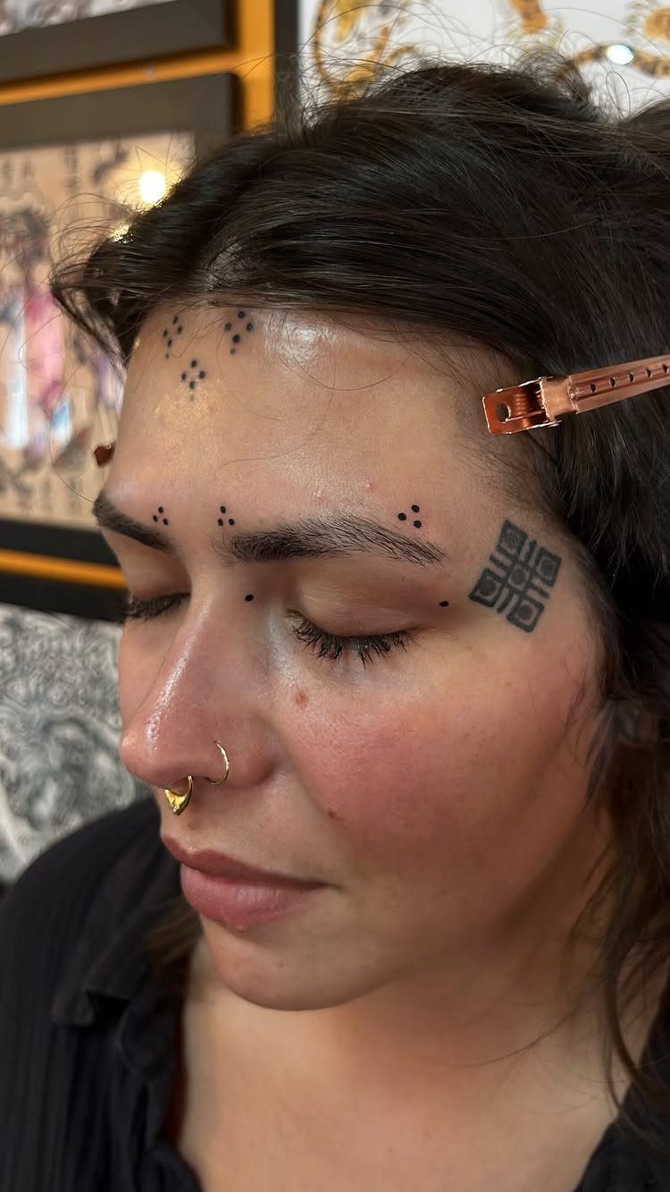 Person with geometric and dot tattoos on their forehead and temple area.