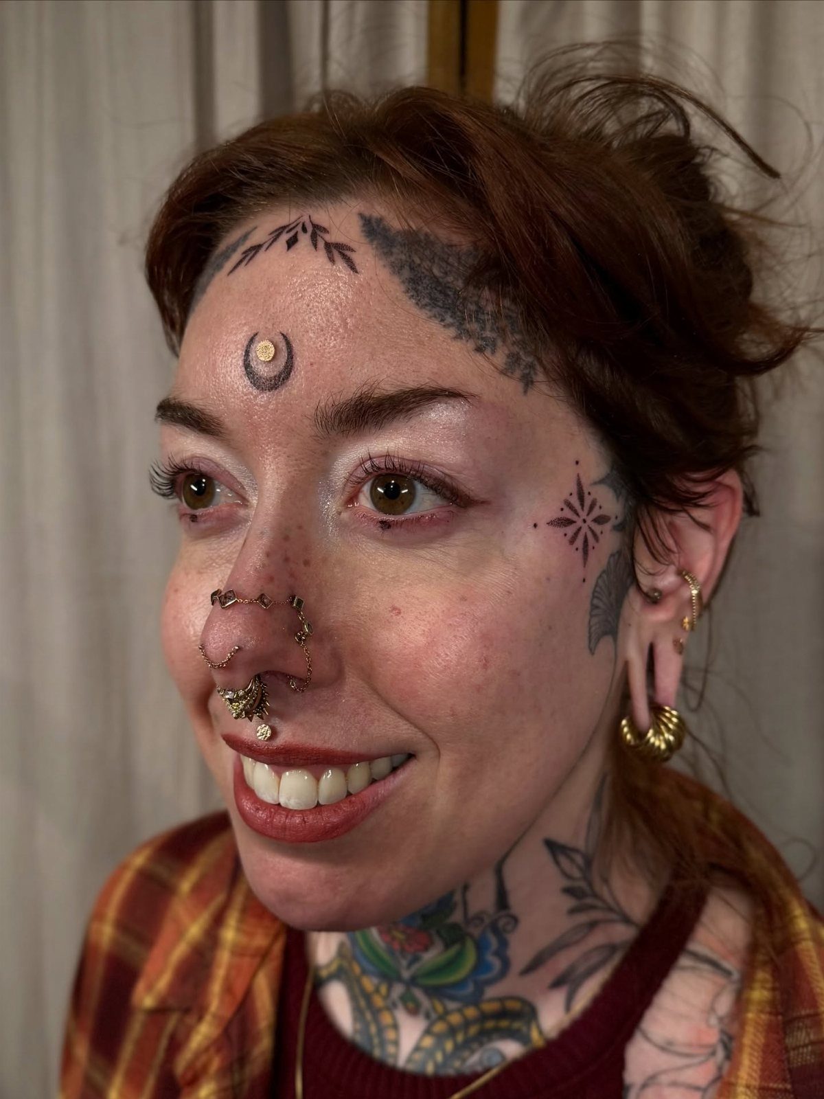 Woman with red hair featuring tattoos on her temple, forehead, and neck.