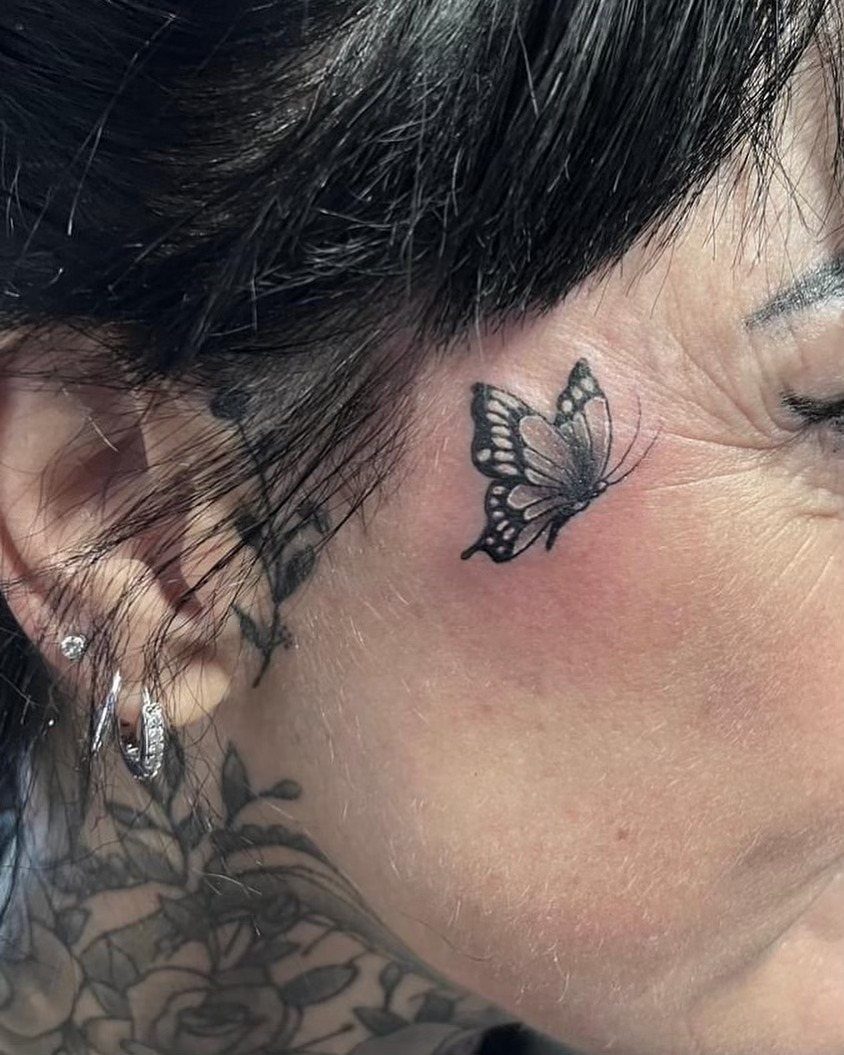 Small black butterfly tattoo on a person's cheek near the eye.