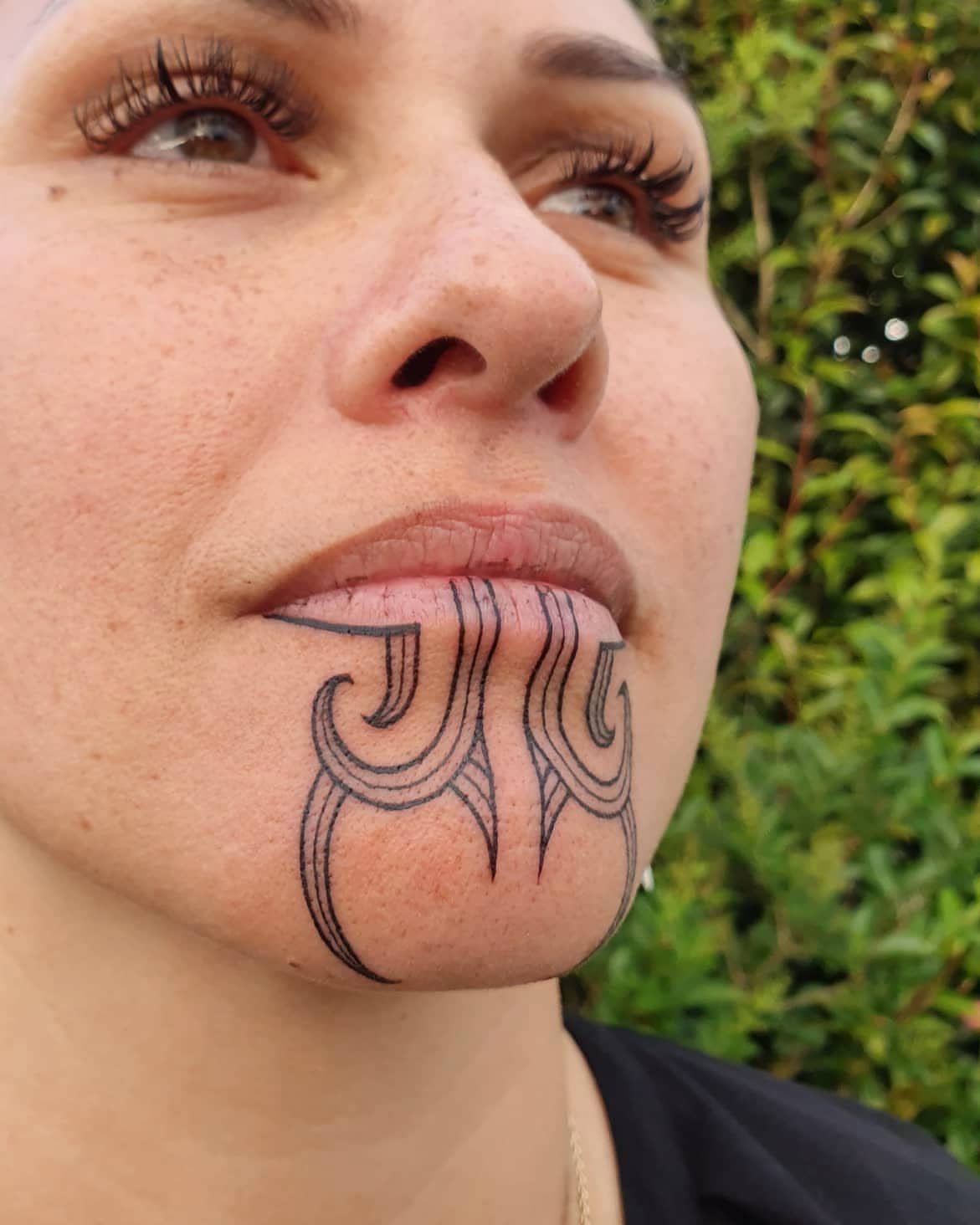 Woman with a black ornamental tattoo on her chin and lower lip.