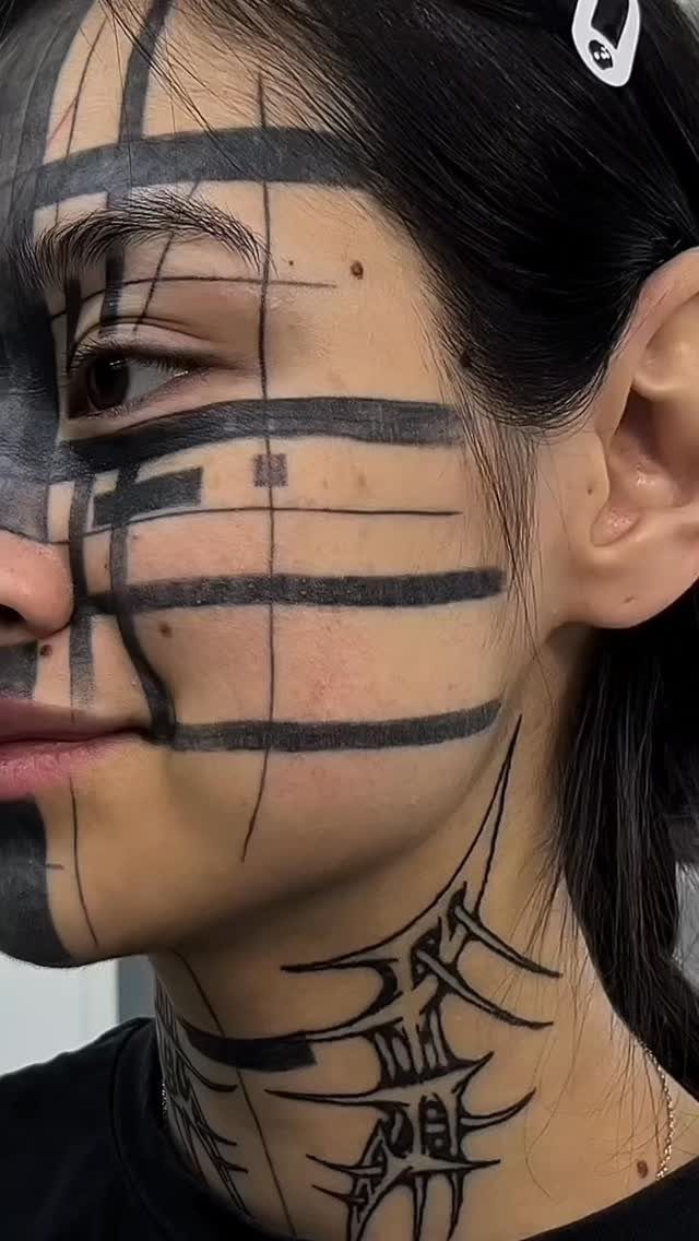 Woman with bold black geometric line tattoos covering her face and neck.