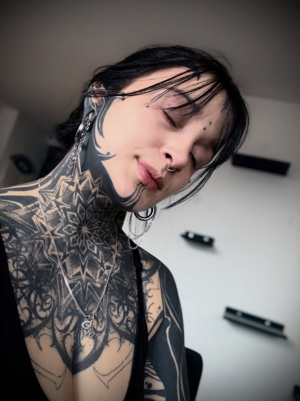 Woman with extensive black ink tattoos including a large mandala on her neck.