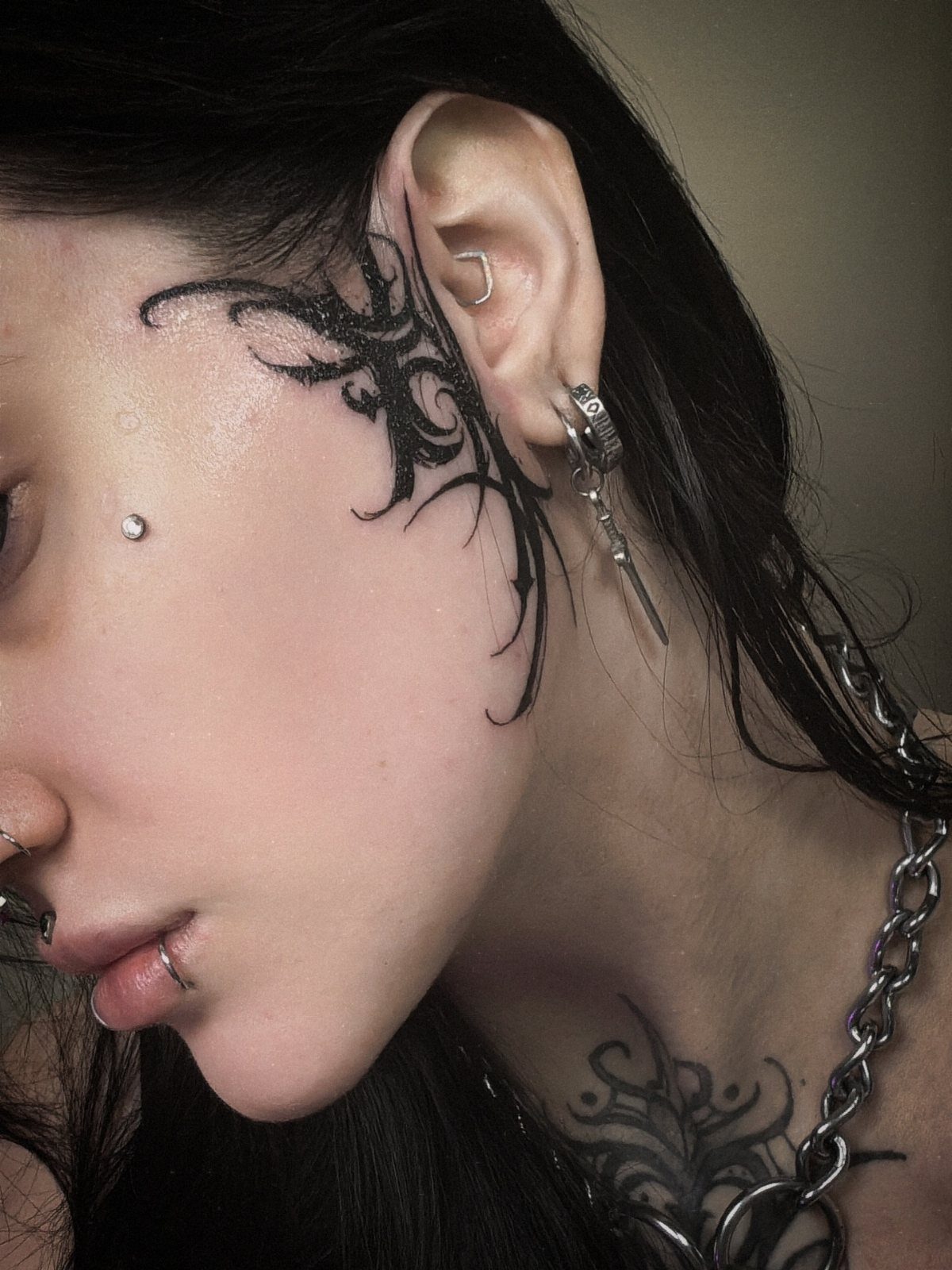 Woman with an intricate black ornamental lace tattoo on her cheek and temple.