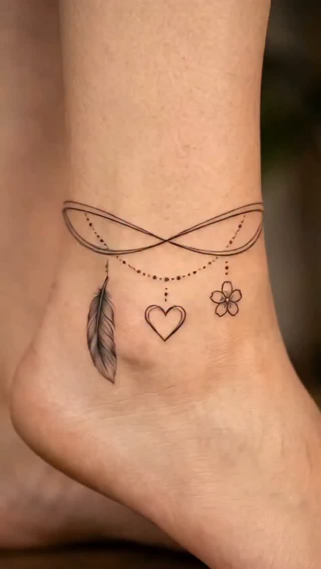 Ankle tattoo featuring an infinity symbol with a hanging feather, heart, and flower.