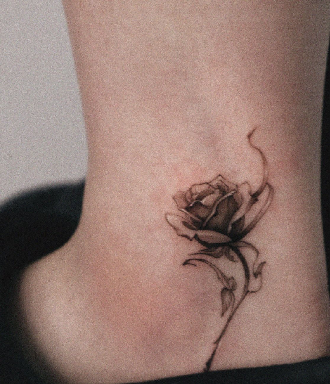 Black and grey rose tattoo on a person's ankle with detailed shading