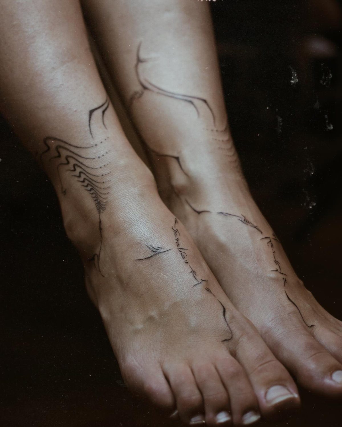 Woman's feet and ankles with abstract black line tattoos in a flowing style