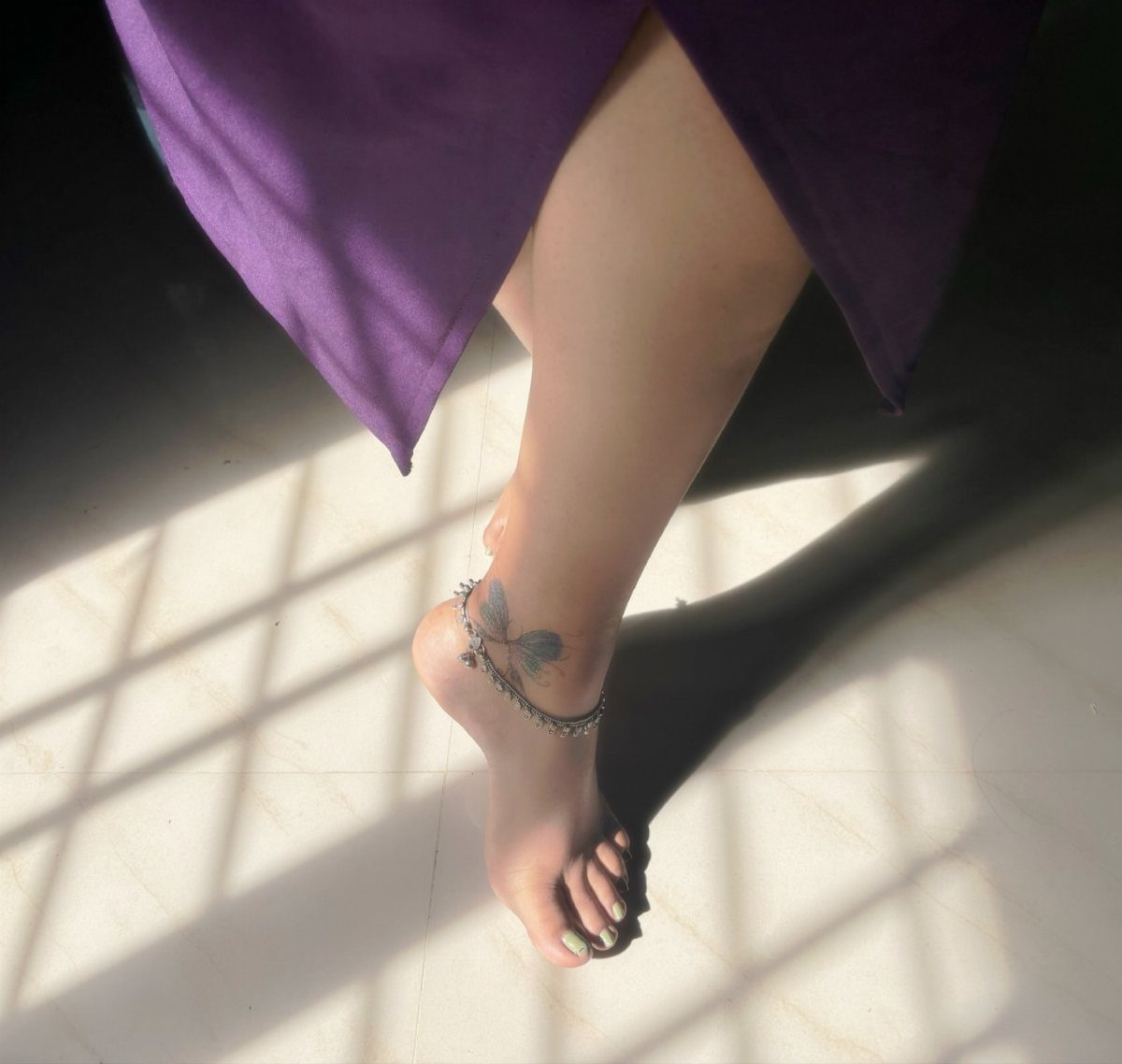 Woman's foot with a blue butterfly tattoo and a silver beaded anklet
