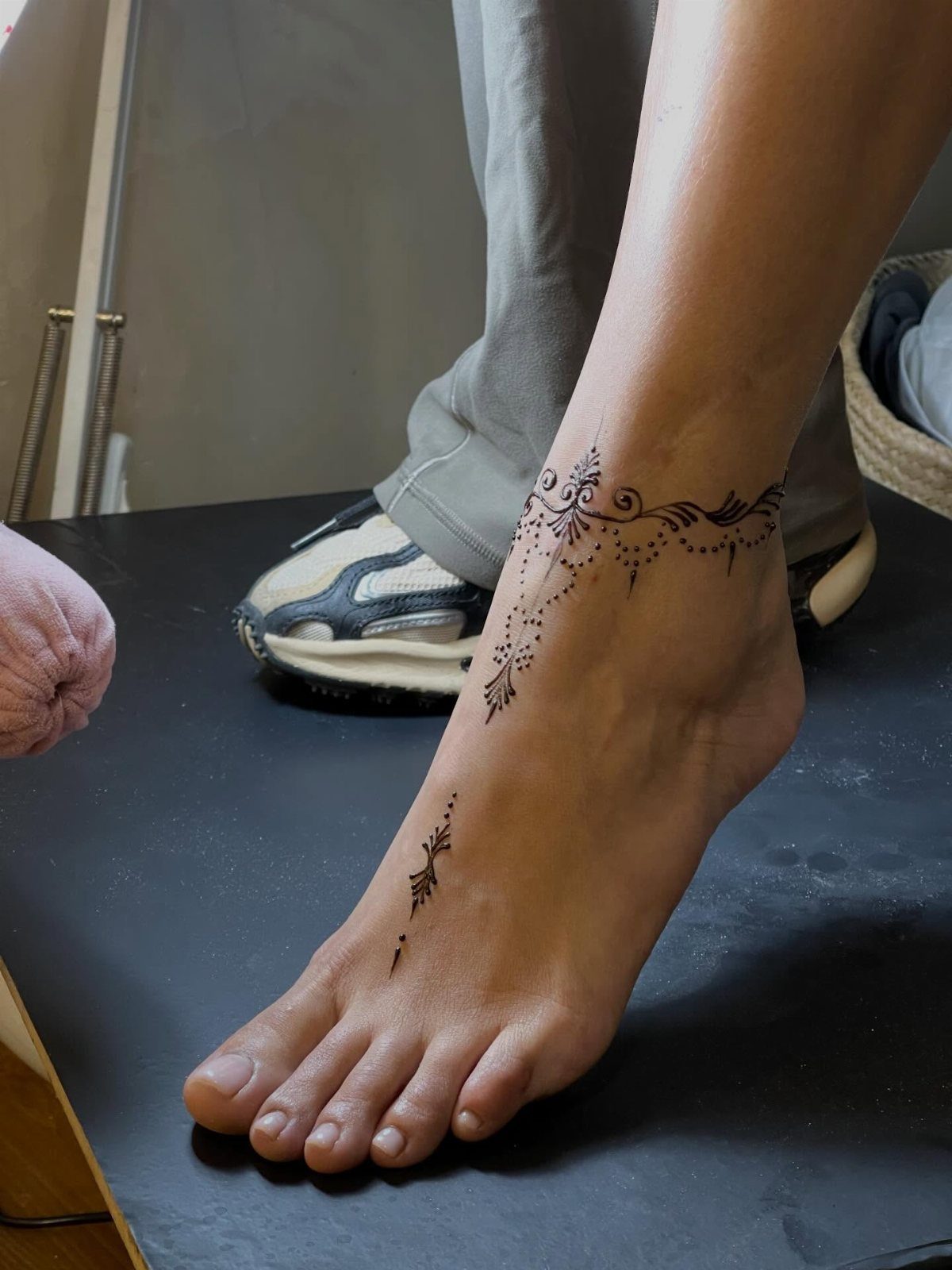Foot and ankle with black henna-inspired ornamental tattoos on a dark background.