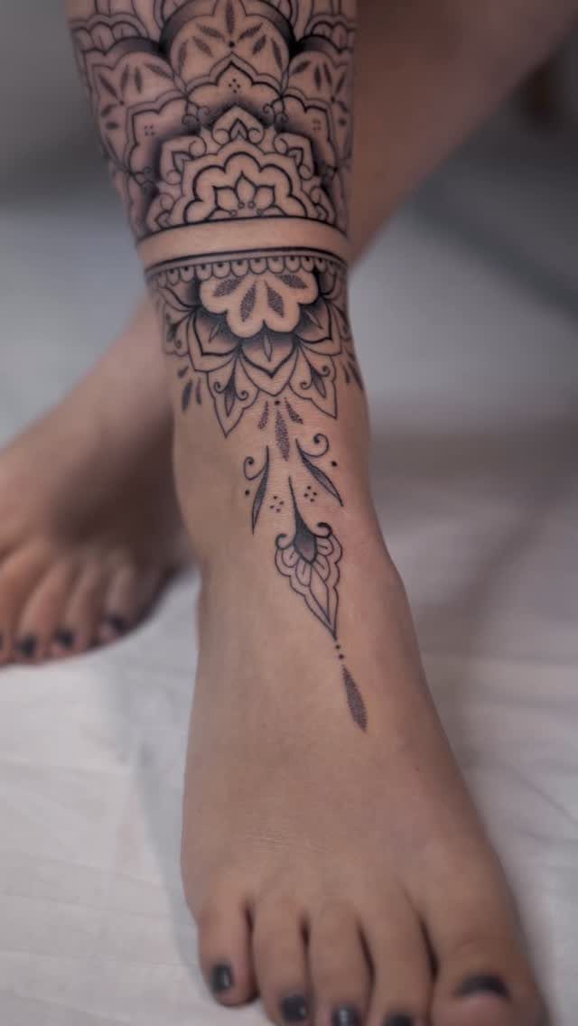 Intricate black ink mandala tattoo wrapping around a woman's ankle and top of foot.