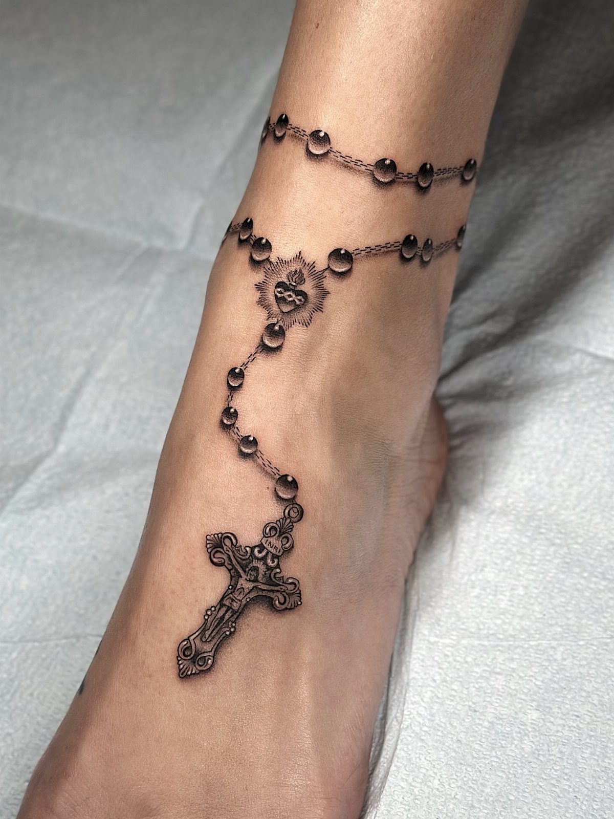 Rosary tattoo with beads and a cross on a woman's foot and ankle.