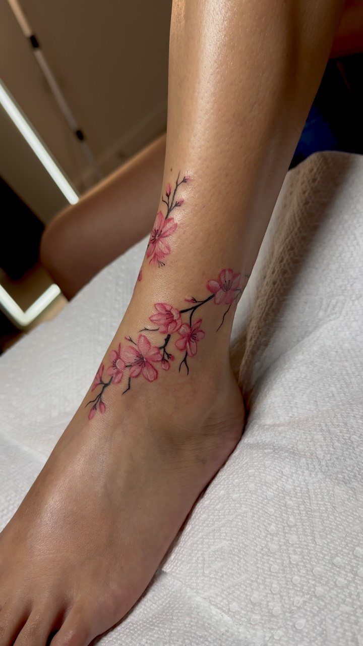 Pink cherry blossom tattoo on a woman's ankle and side of the foot.