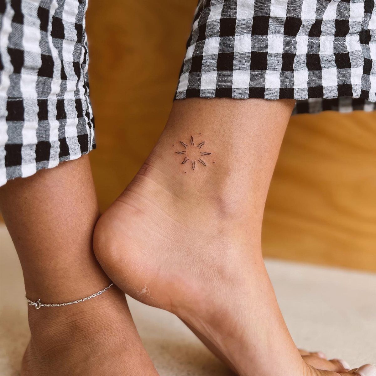Small sun tattoo on a person's ankle with black and white checkered pants.