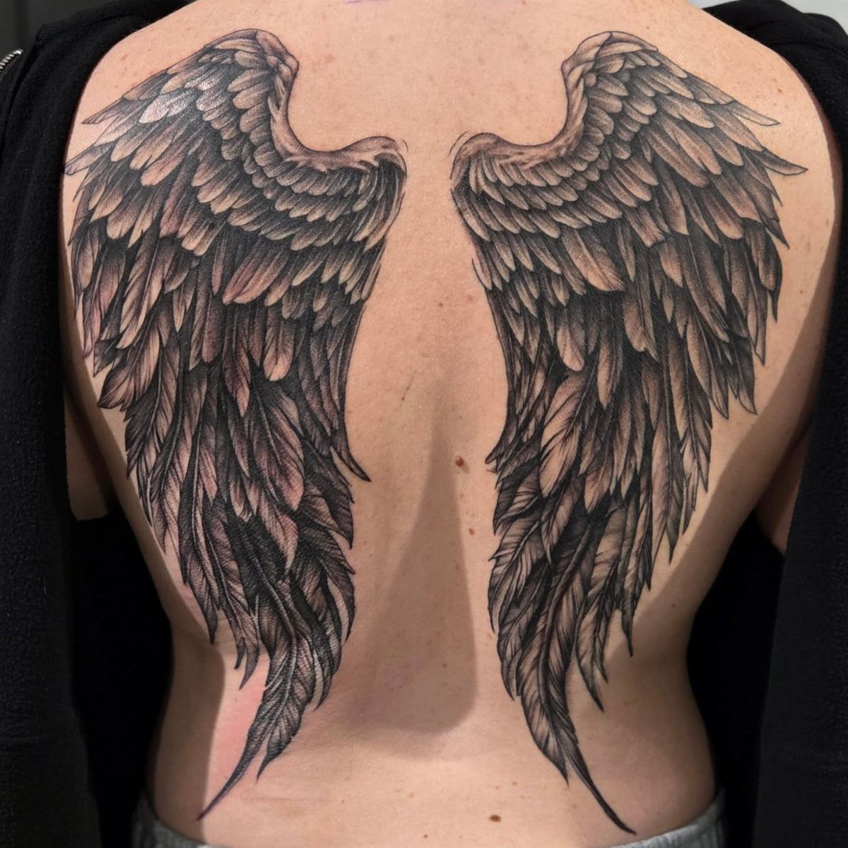 Detailed black and grey angel wings tattoo covering a person's entire back.