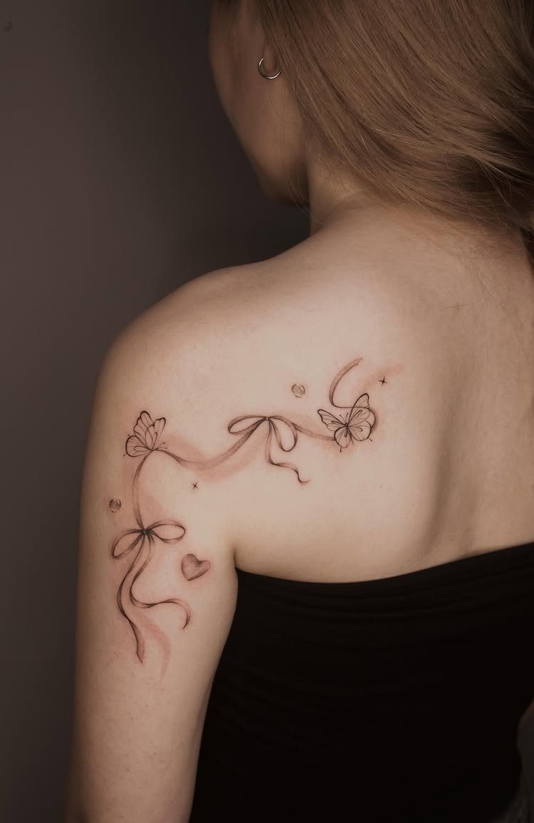 Butterfly tattoo with ribbons and bows on a woman's upper back and shoulder.