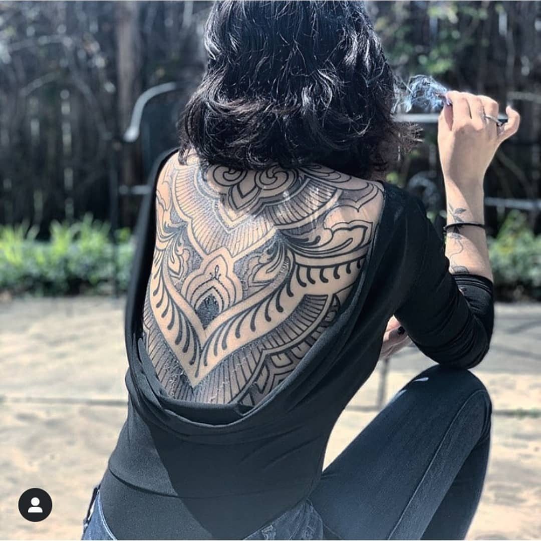 Symmetrical black ink geometric tattoo on a person's upper back