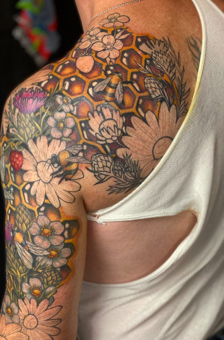 Honey bee and floral tattoo with honeycomb patterns on a person's shoulder.