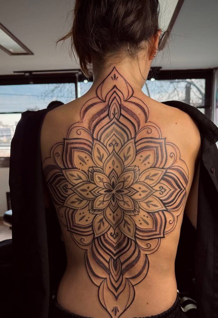 Intricate mandala tattoo centered on a woman's back with symmetrical geometric patterns.