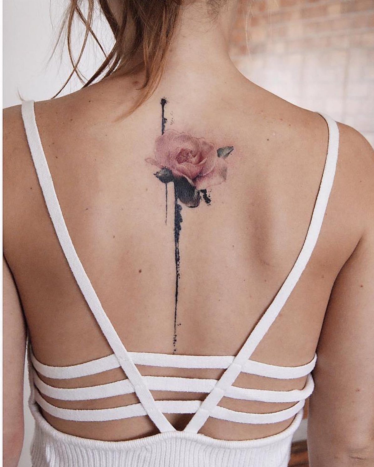 Pink rose tattoo with a vertical black line on a woman's spine.