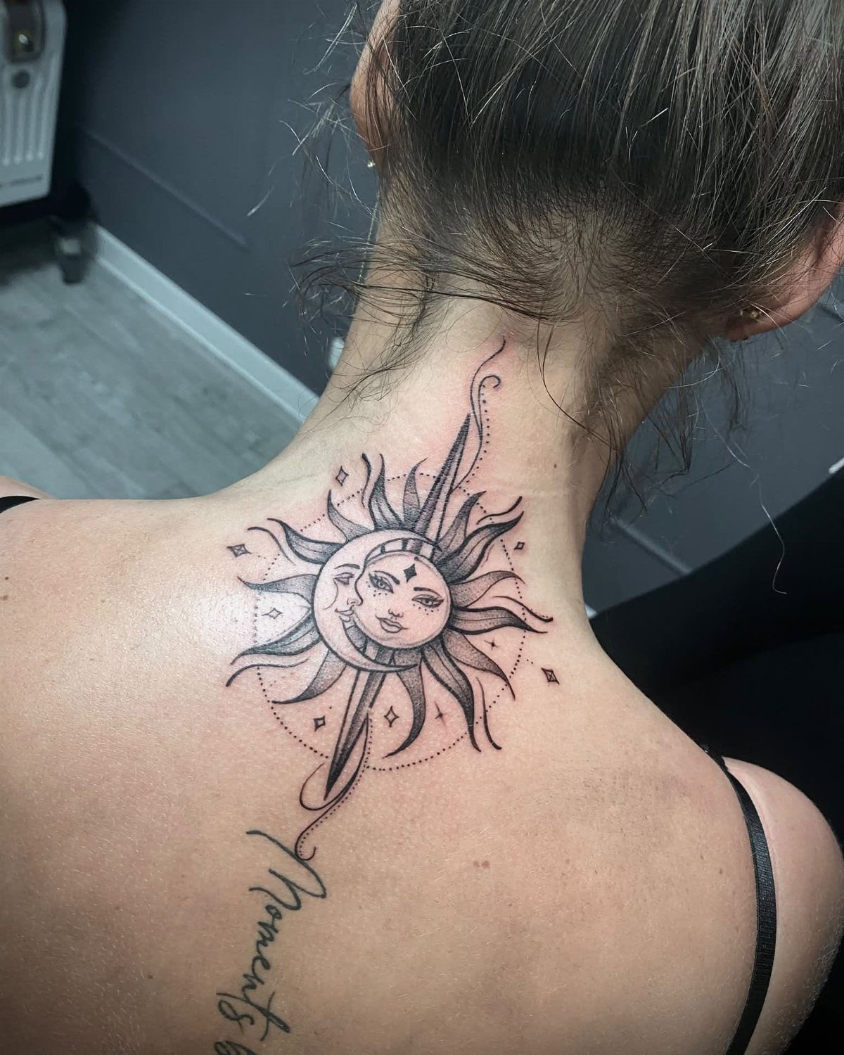Sun and moon tattoo with faces on a woman's upper back and neck.