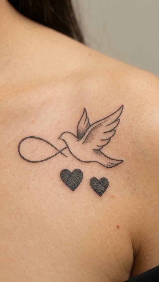 Dove and infinity symbol tattoo with two hearts on a person's shoulder