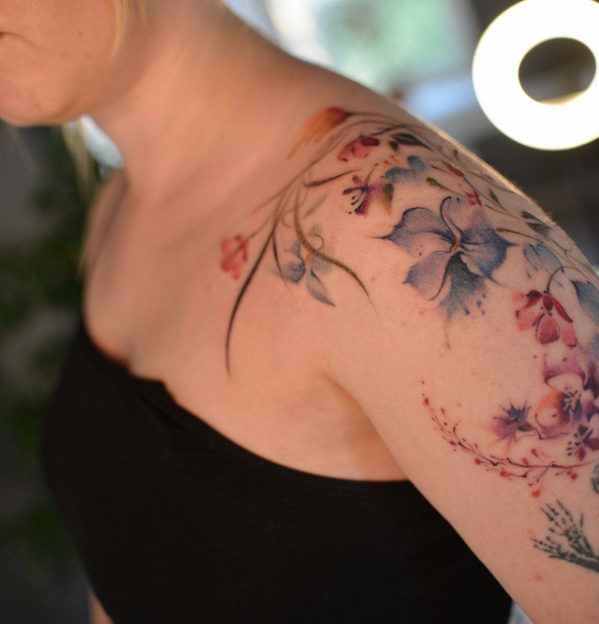 Watercolor floral tattoo with blue and pink blossoms on a person's shoulder