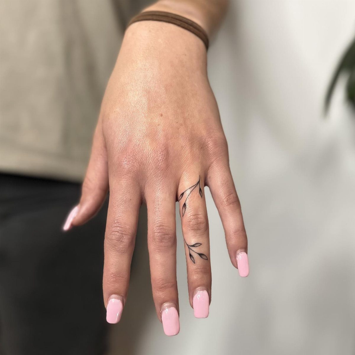 Hand with pink nails featuring a fine line leaf branch tattoo on finger