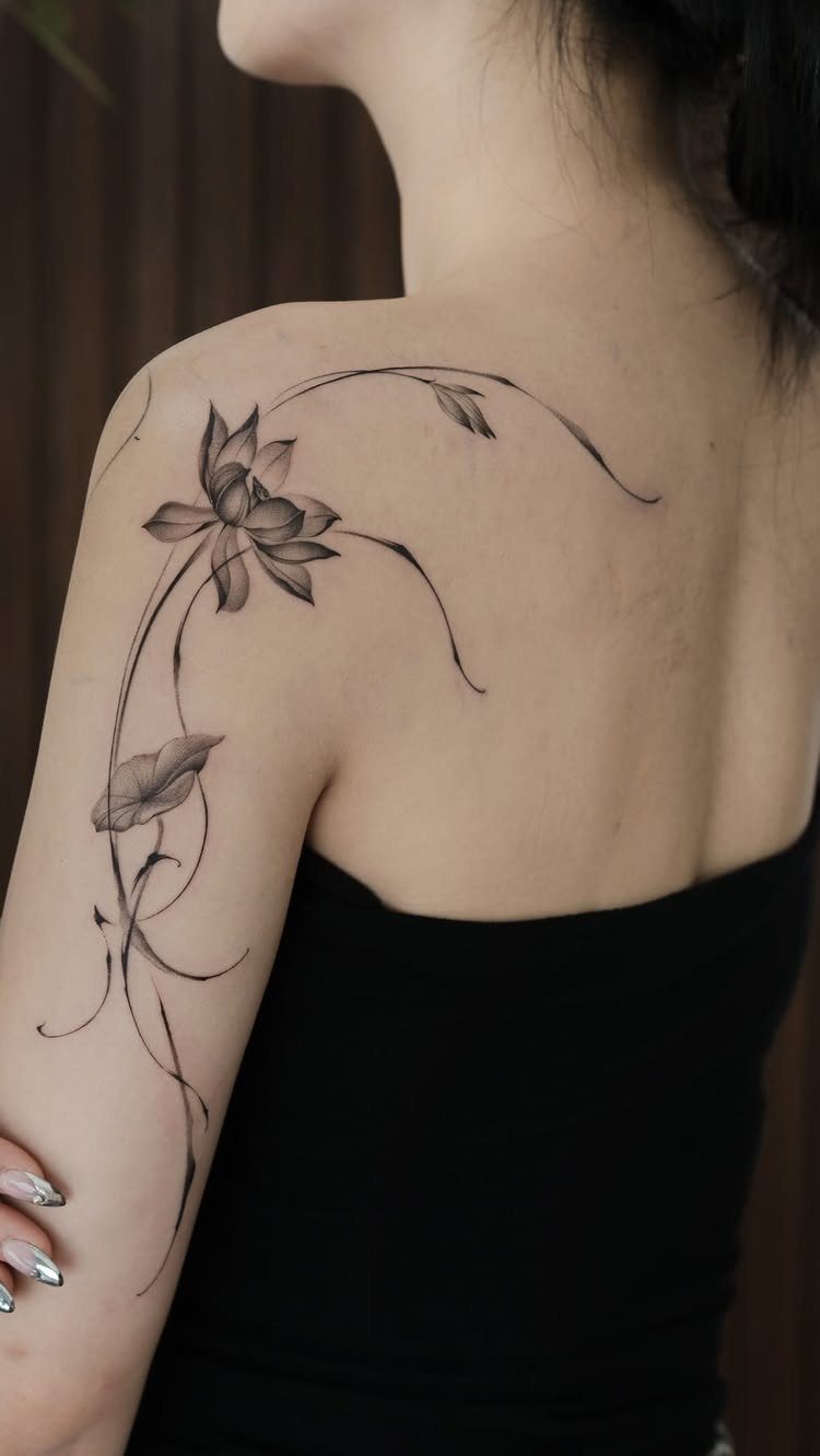 Lotus flower fine line tattoo on a woman's shoulder and upper arm.