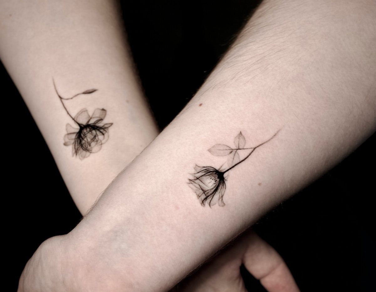 Two fine line rose tattoos on the inner wrists of two people.