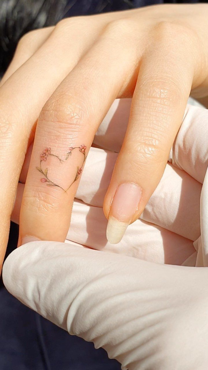 Small heart tattoo made of floral vines on a person's finger