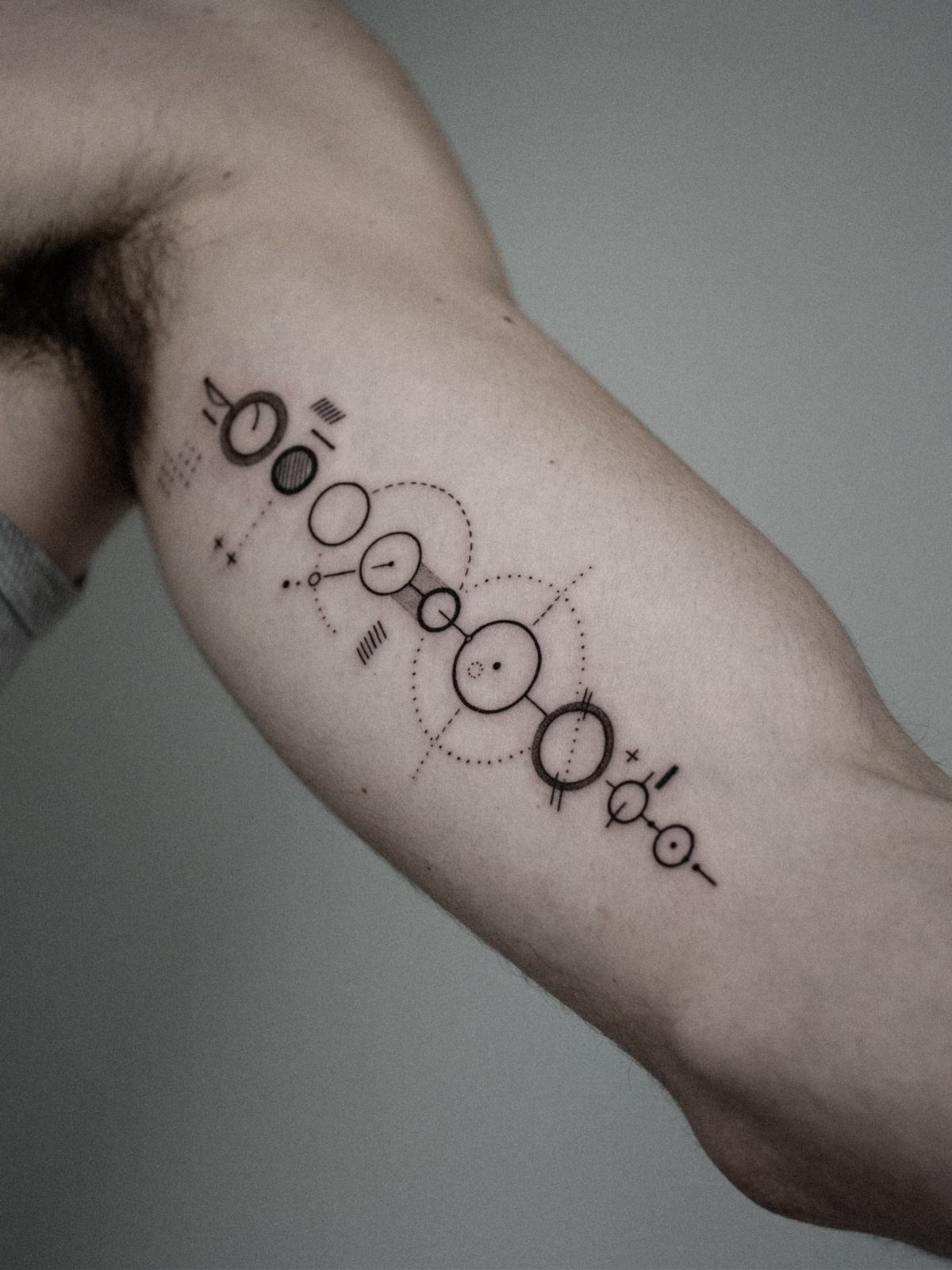 Abstract geometric line tattoo with circles and dots on a man's upper arm.