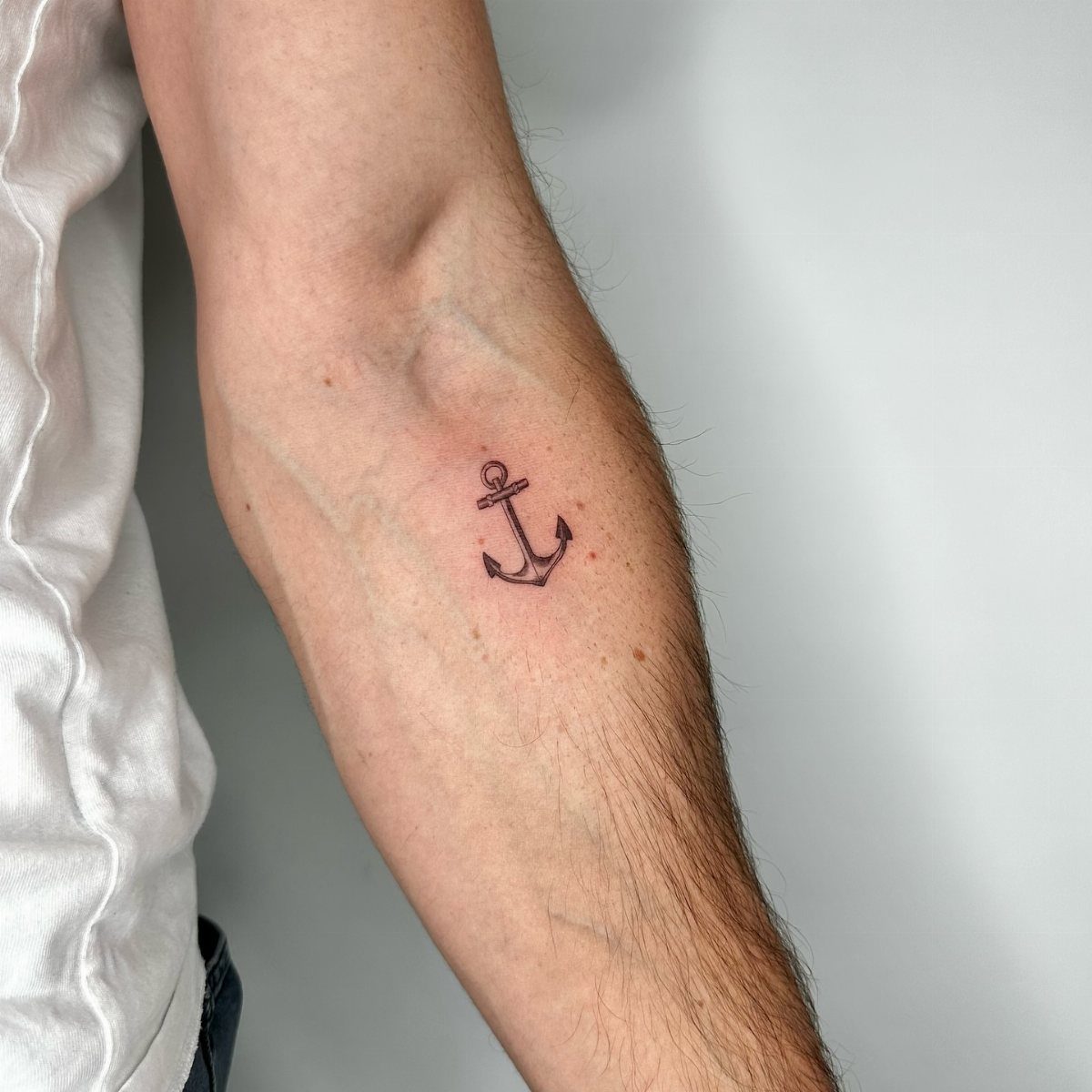 Small black fine-line anchor tattoo on a man's inner forearm.