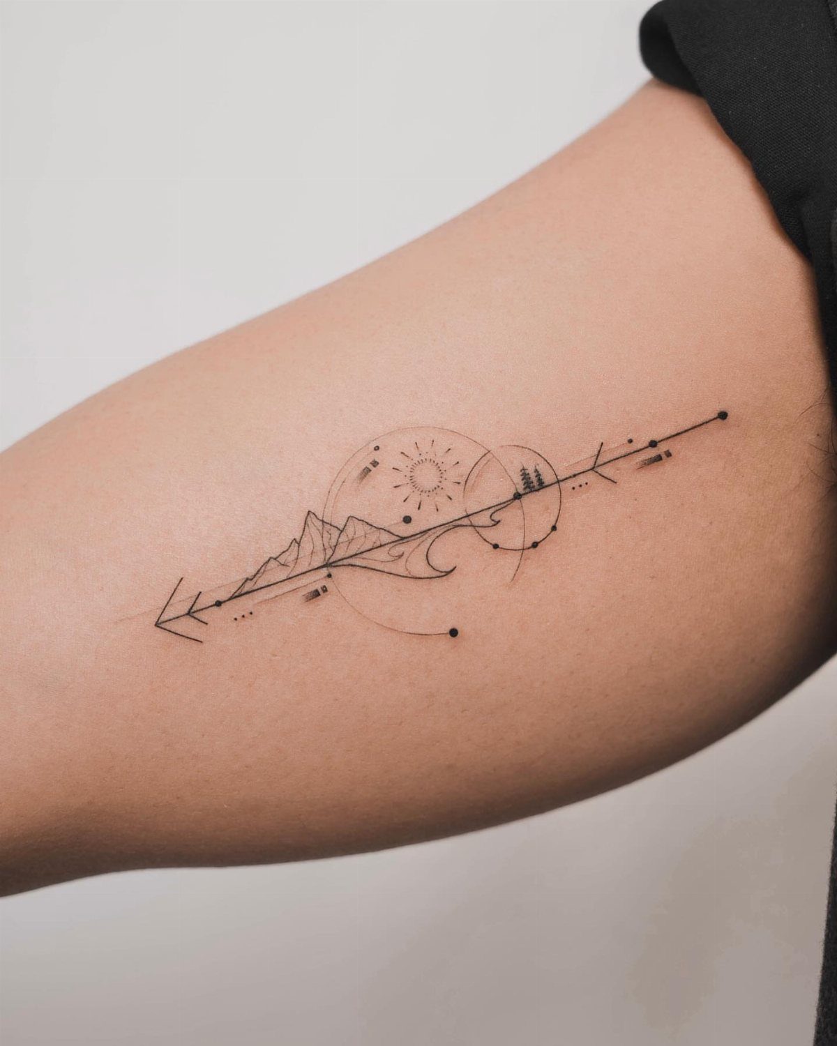 Fine line tattoo on an arm depicting mountains, a sun, and an arrow.