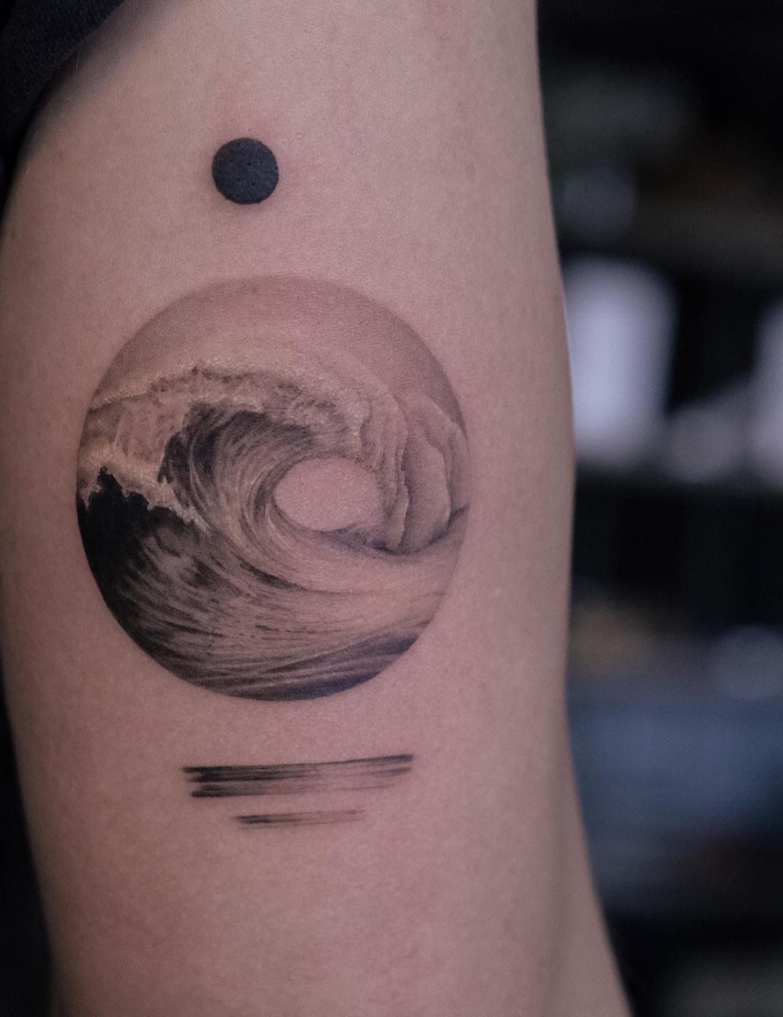 Circular ocean wave tattoo with a black dot and lines on an arm