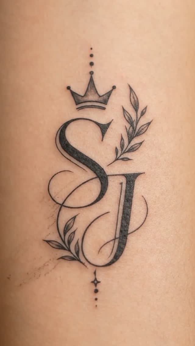 Intertwined script initials S and J tattoo with a crown and leafy accents.