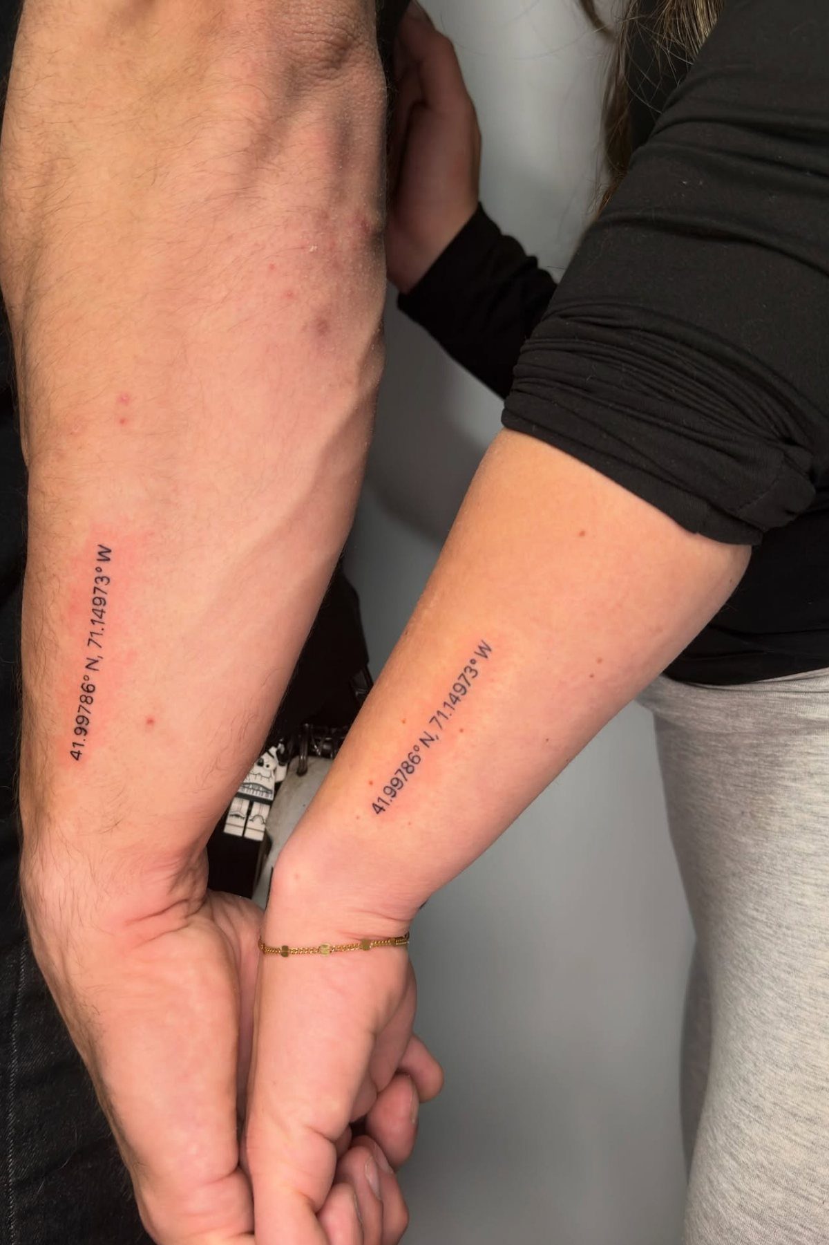 Matching geographic coordinates tattoos on a man's forearm and a woman's wrist.