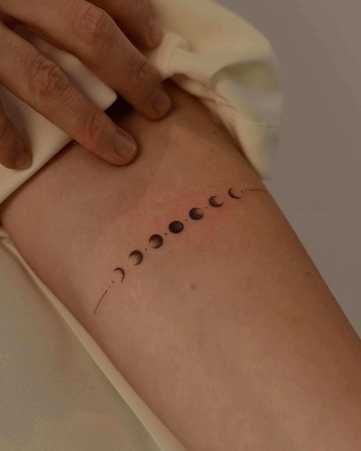 Lunar phase tattoo on a forearm with a white sleeve being lifted.