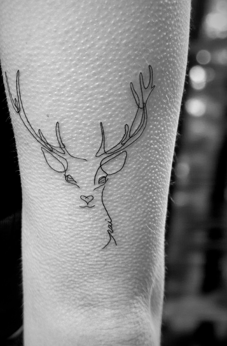 Minimalist deer silhouette tattoo with fine lines on a person's arm.