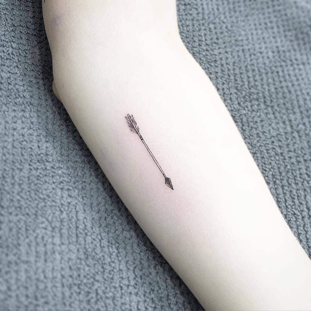 Small black fine line arrow tattoo on a person's pale forearm