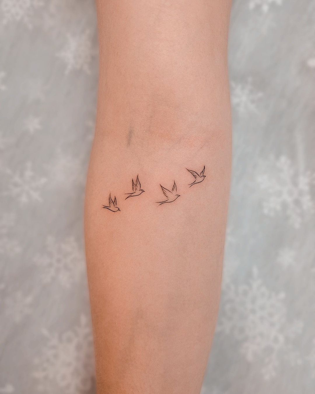 Four small fine line bird tattoos in flight on a person's forearm