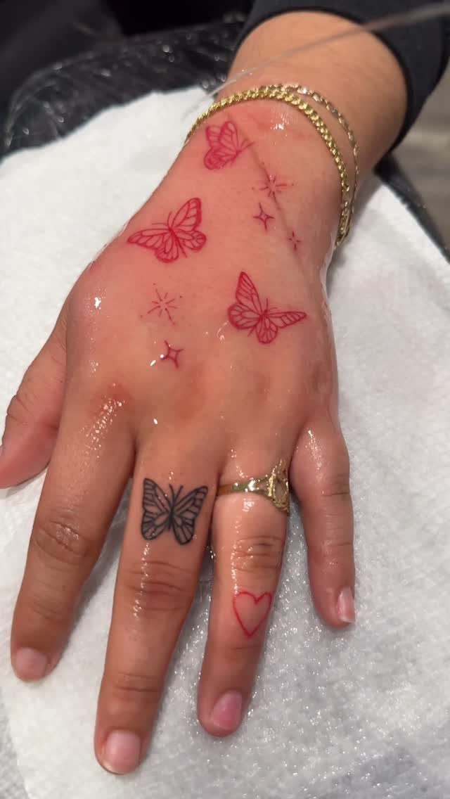 Hand with black butterfly finger tattoo and red butterfly tattoos on the skin