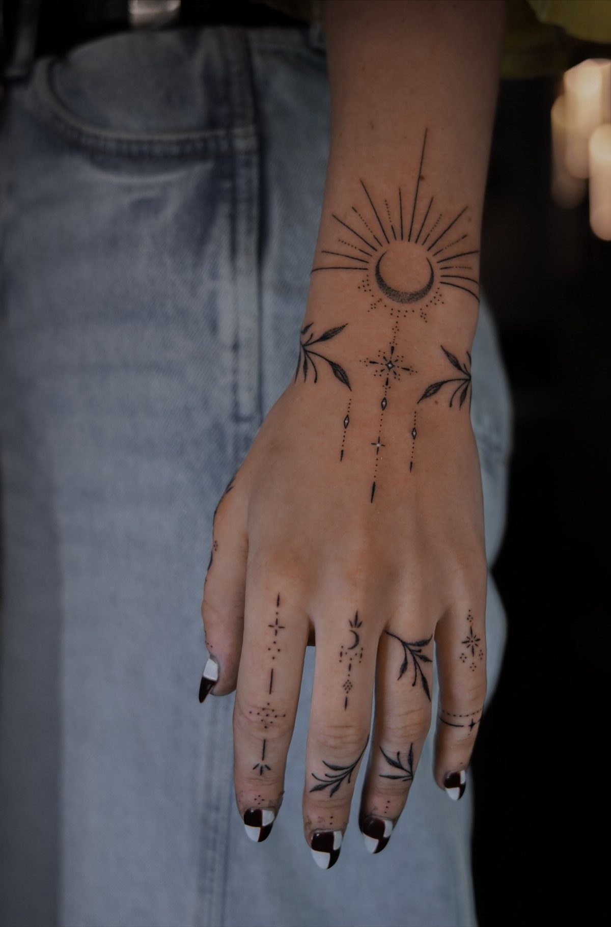 Hand and wrist with celestial and botanical black ink tattoos including a crescent moon.