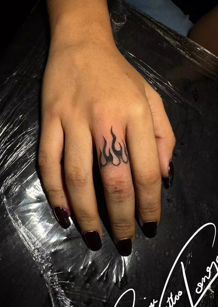 Hand with a black flame tattoo on the middle finger and dark nails.