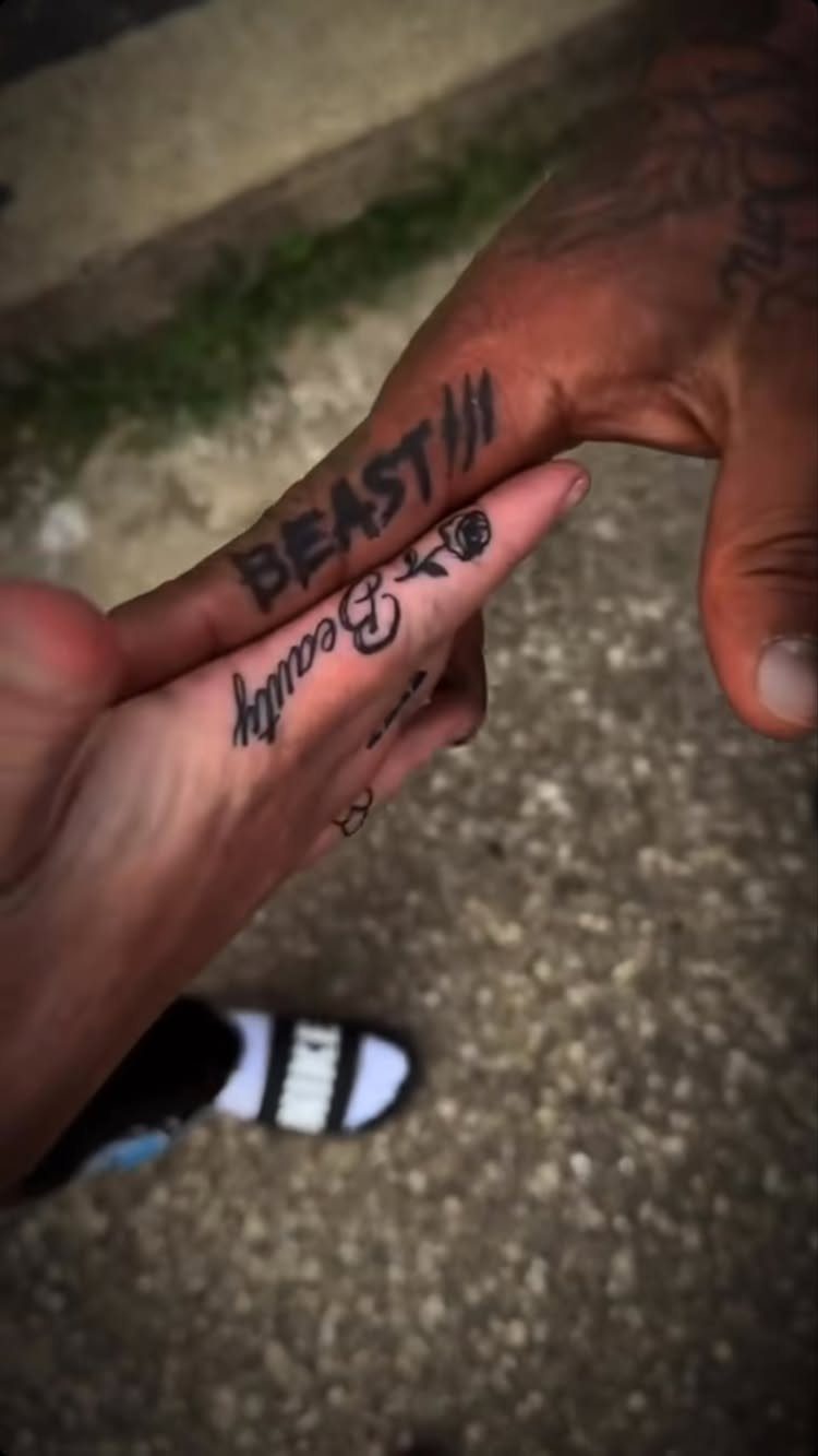 Two fingers with matching Beast and Beauty tattoos held together against a pavement.