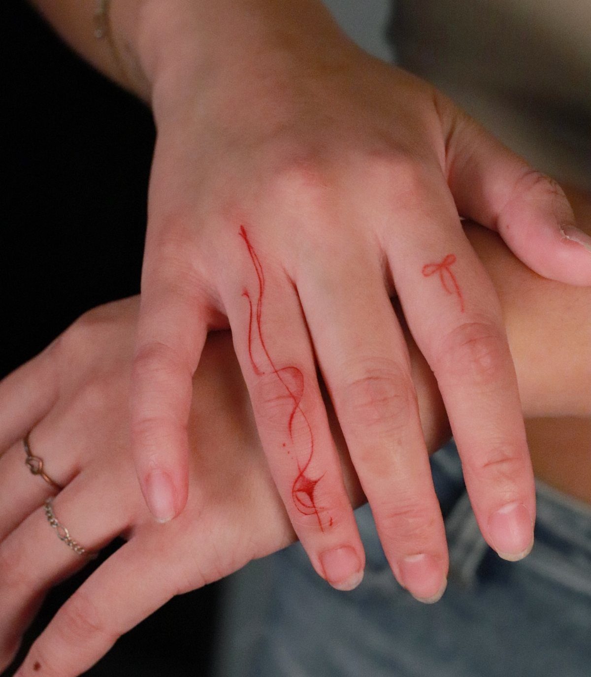Red ink tattoos of a swirling vine and a small bow on fingers