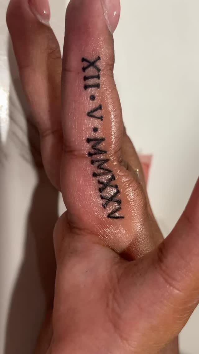 Roman numeral tattoo inked vertically on the side of a person's finger.