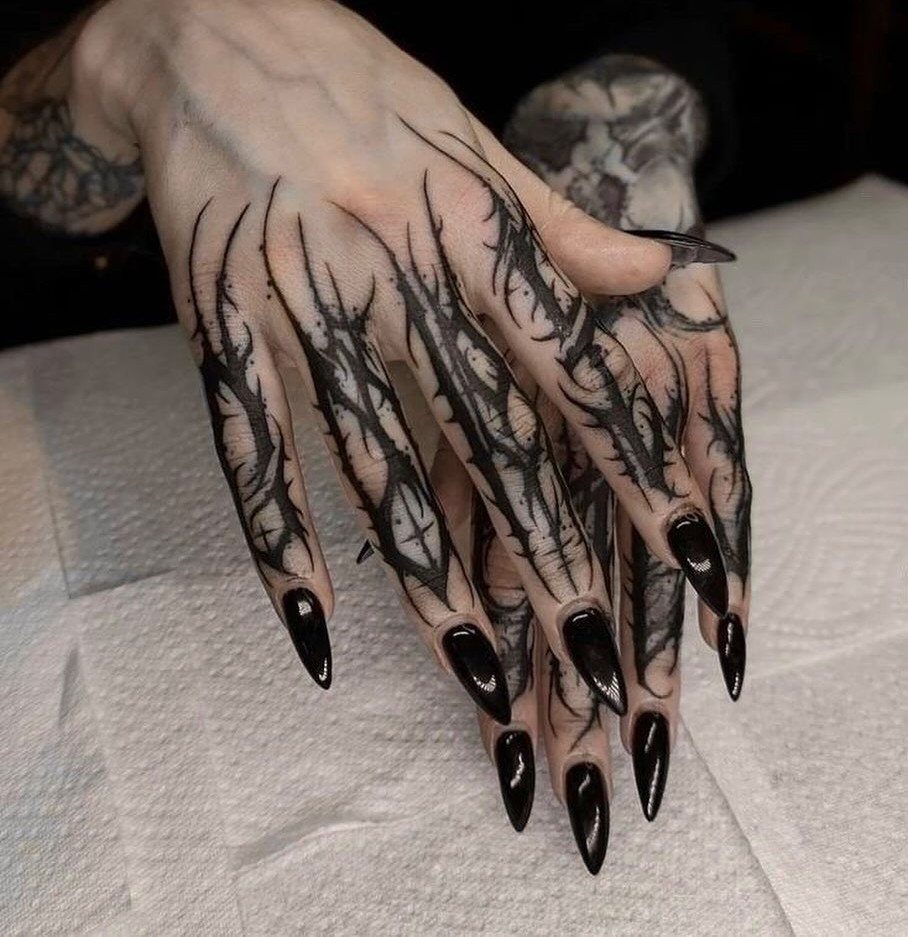 Hands with bold black abstract finger tattoos and long pointed black nails.