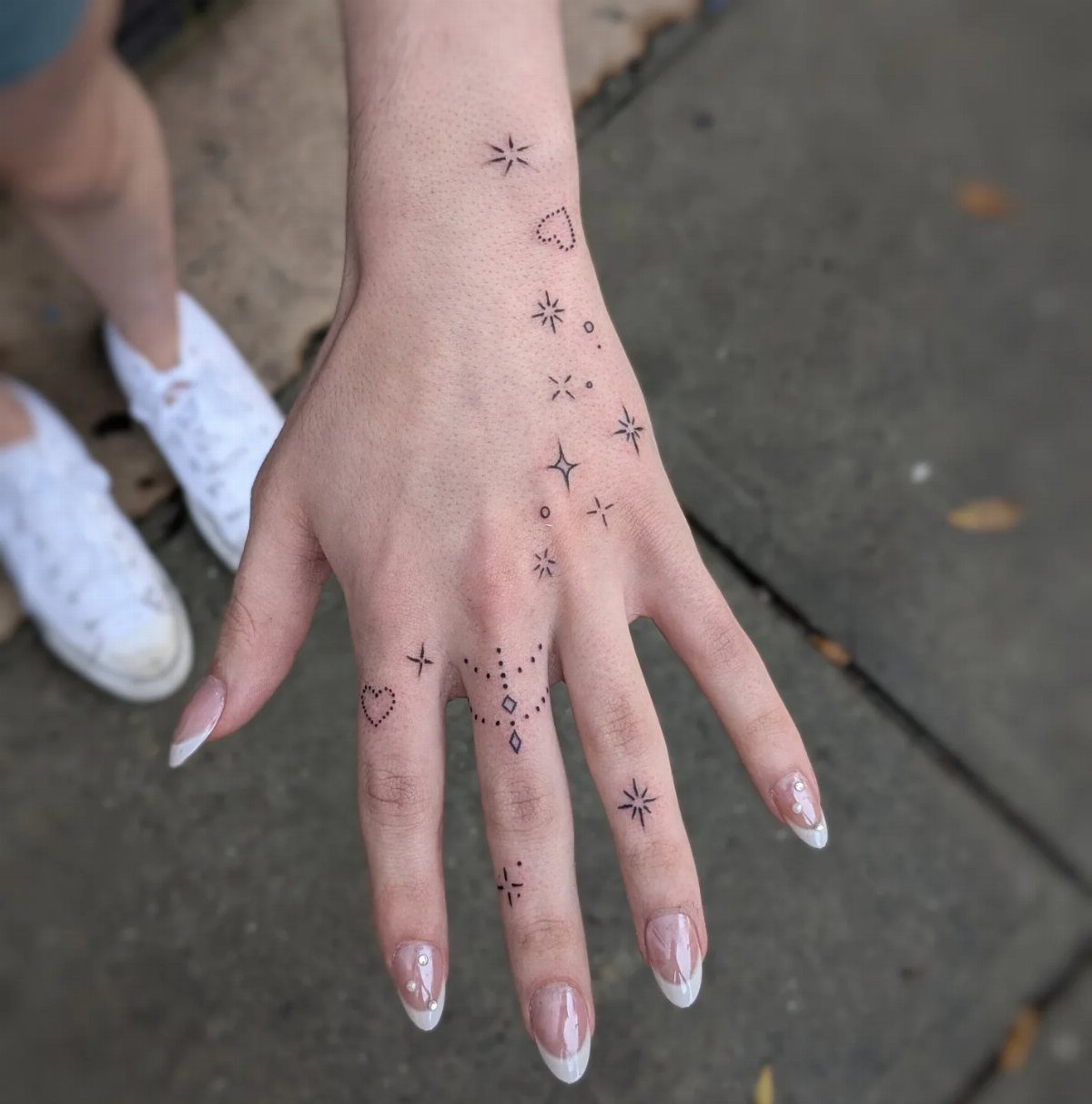 Hand with small black ink star and heart tattoos on fingers and wrist