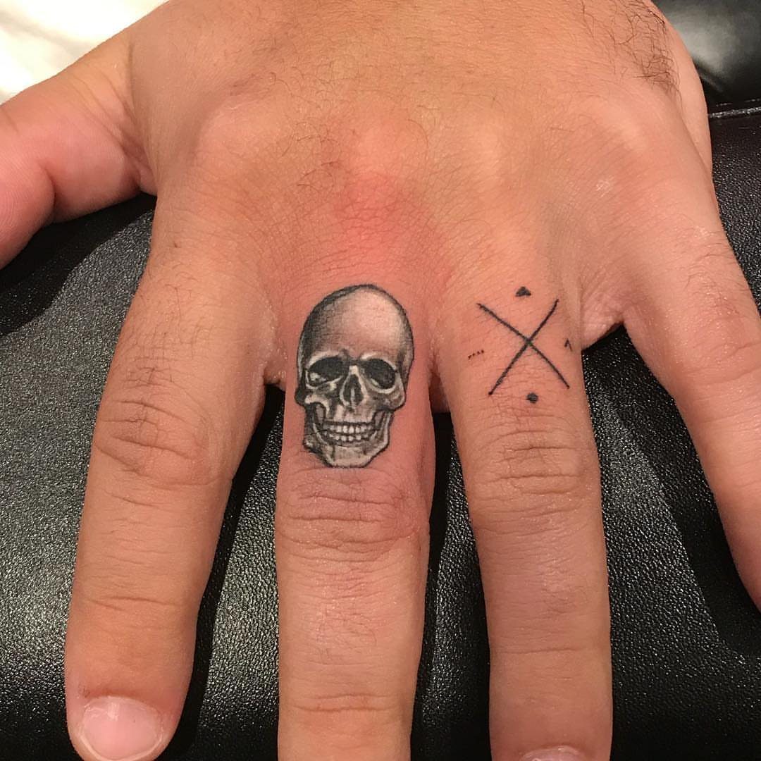 Detailed black and grey skull tattoo on a person's middle finger